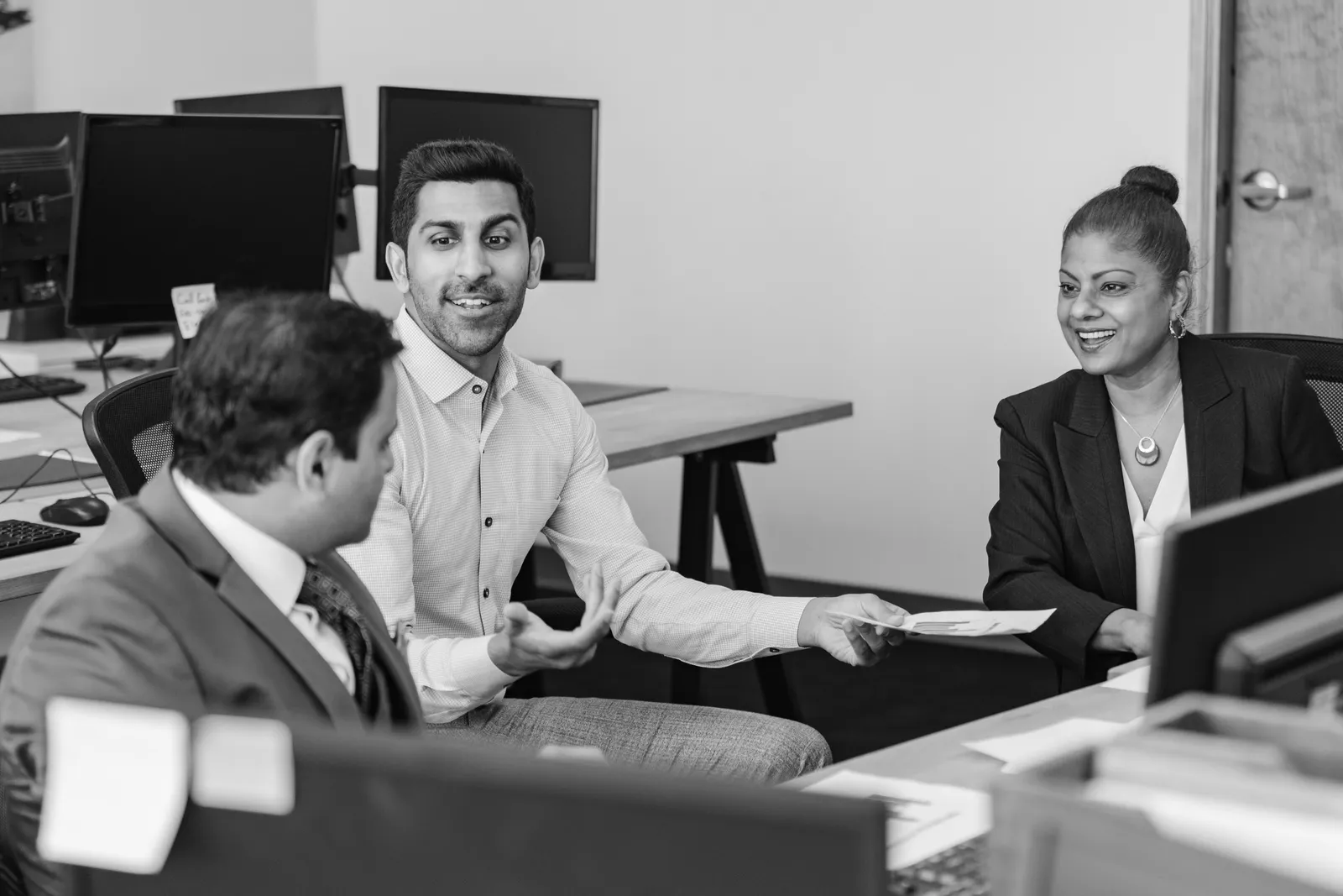Three colleagues in conversation at their desks