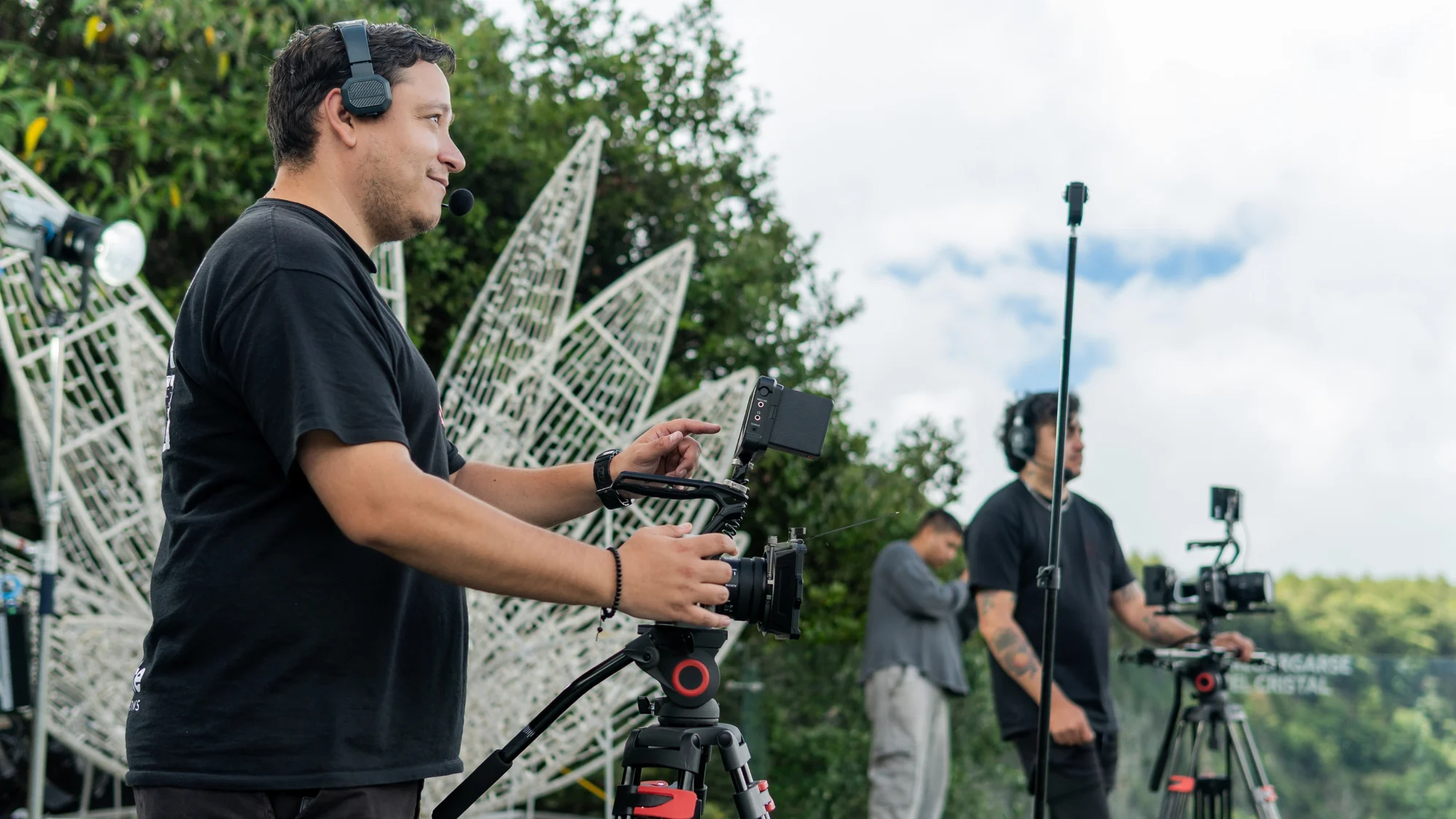 A film crew with headsets and cameras on tripods, shooting outdoors