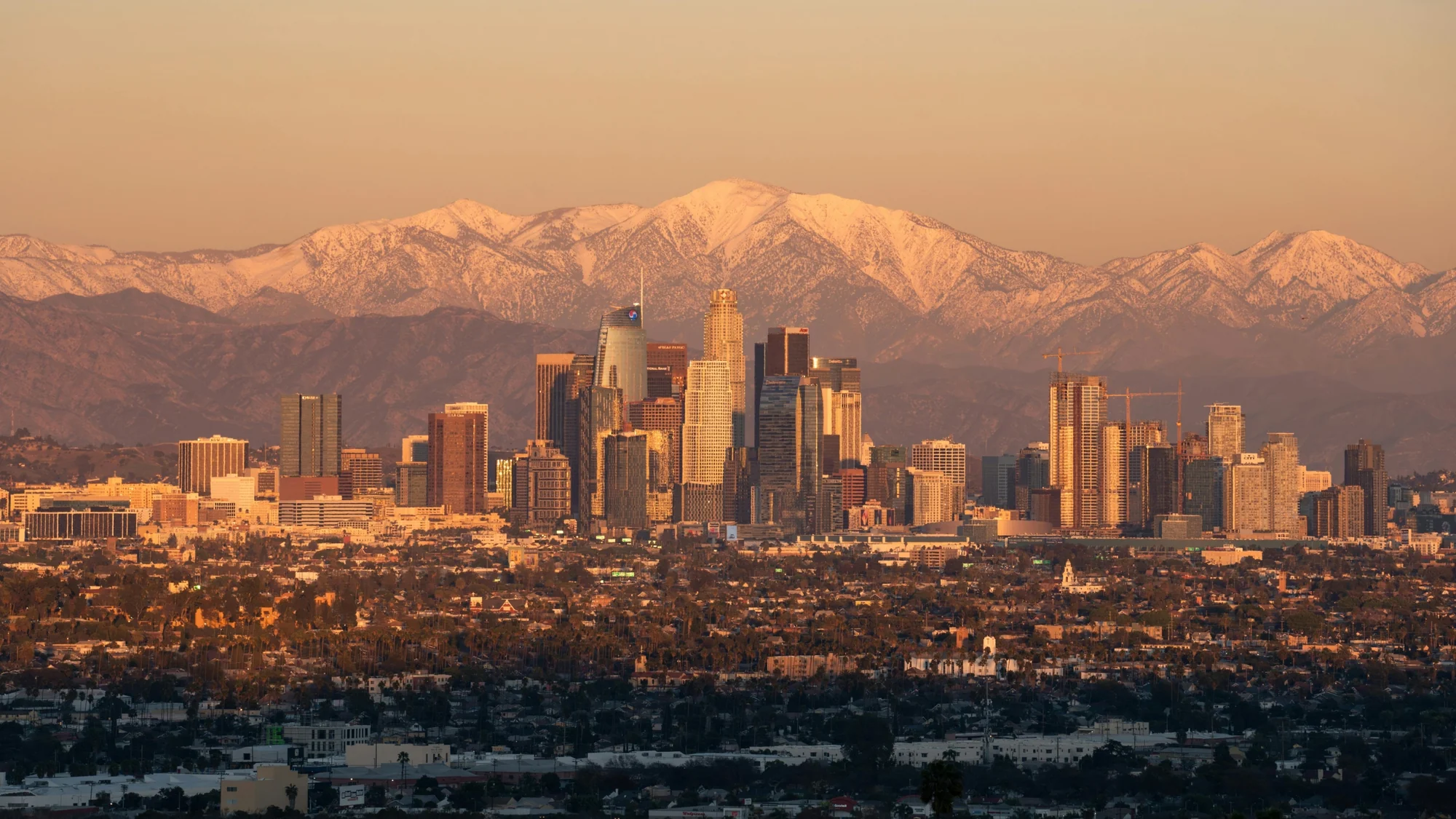 Downtown Los Angeles towers lit by late sun, snow-capped mountains behind